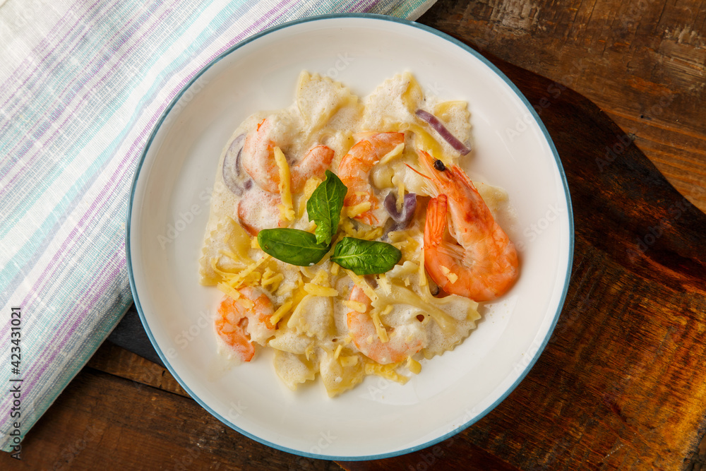 Pasta with shrimps in a creamy sauce on a gray plate on a wooden table on a napkin.