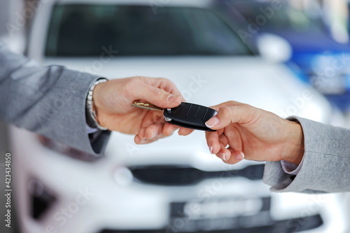 Car seller handing car keys to a customer while standing in car salon.