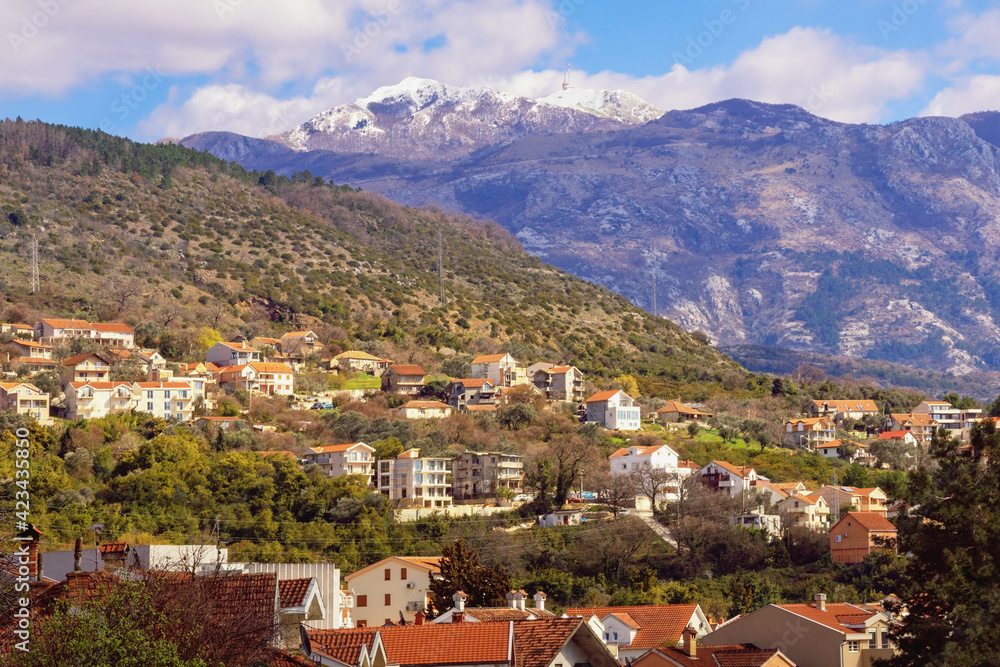 Beautiful mountain landscape on sunny spring day. Green town at foot of mountains. Montenegro, view of snow-capped peaks of Lovcen mountain and Tivat town