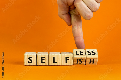 Selfish or selfless symbol. Businessman turns cubes and changes the word 'selfish' to 'selfless'. Beautiful orange background, copy space. Business, psuchological and selfish or selfless concept. photo