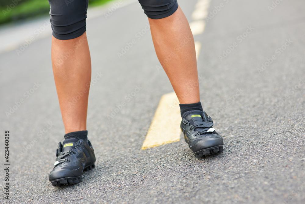 Close up shot of legs of professional male cyclist wearing cycling shoes, standing on the road outdoors