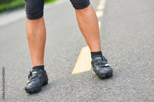 Close up shot of legs of professional male cyclist wearing cycling shoes, standing on the road outdoors