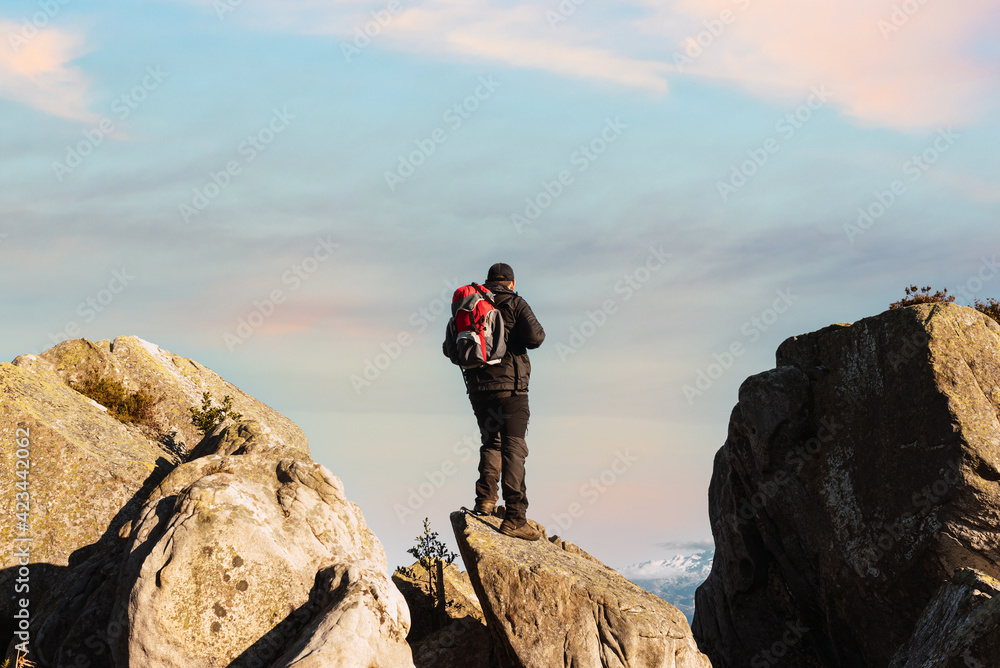 mountaineer posing on the rocks of a mountain at sunset. hiker contemplating the landscape weekend getaway. single person exercising. mountain activities.