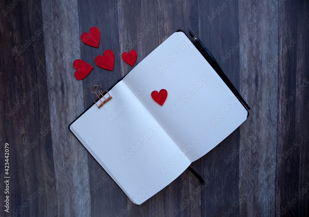 Top view of a blank   dot grid notebook  surrounded by heart shapes