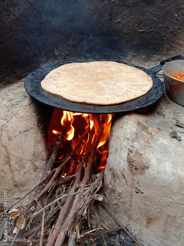 wooden fire burning in hand made mud stove with bread (roti) is being baked on desi tawa ,village