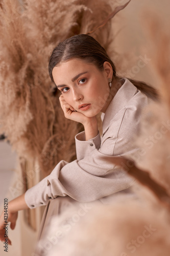 Fall fashion portrait. Brunette girl with pony tail and natural makeup. Elegant woman posing between ears of rye at textile background. Stylish female model in brown skirt anf beige jacket