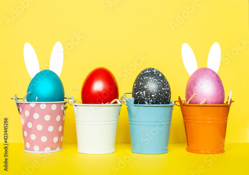 colored Easter eggs in bright buckets with bunny rabbit ears,   selective focus image. Happy Easter card.	
