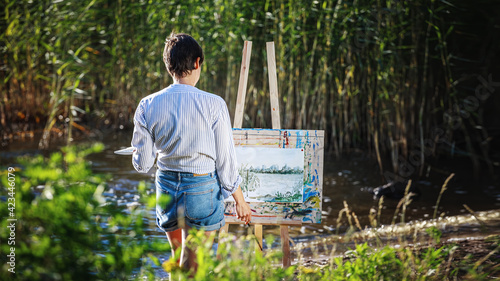 Photo A female artist paints a watercolor painting on the shore of a lake among reeds