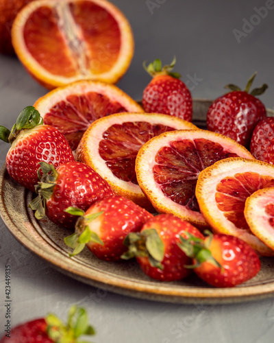 Plate of fruits with sliced red orange and strawberry on grey background, Vitamin fruits concept, selective focus