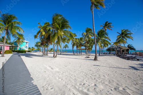 Tropical white sand beach with coco palms and the turquoise sea on Caribbean island.  Pastel color houses pink, green, blue.  Little Cayman, Cayman Islands © Iconic