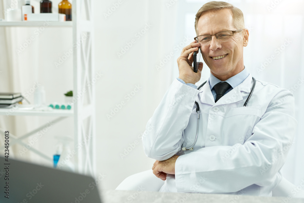 Joyful male doctor having phone conversation in clinic Joyful male doctor having phone conversation in clinic
