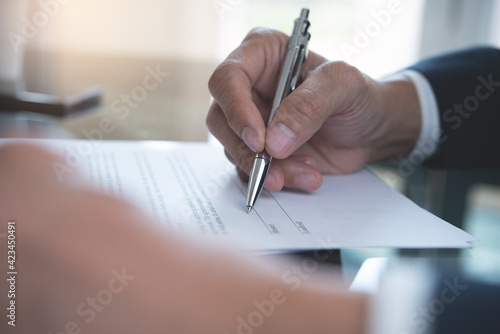 Close up of businessman hand with a pen signing business contract, paper document on table at office