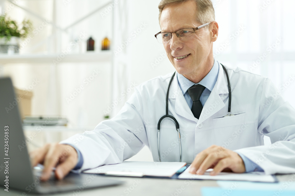 Cheerful doctor using modern notebook in clinic Cheerful doctor using modern notebook in clinic
