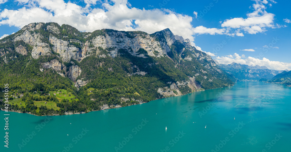 Aerial drone shot over beautiful Walensee  lake, Switzerland, with the view to Seerenbach waterfalls and boats and yacht sailing through turquoise waters of lake