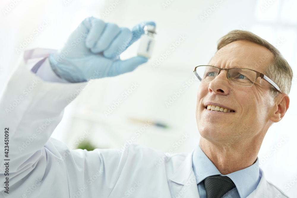 Cheerful male doctor in glasses holding bottle of vaccine Cheerful male doctor in glasses holding bottle of vaccine