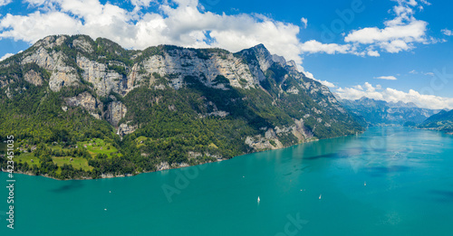 Aerial drone shot over beautiful Walensee lake, Switzerland, with the view to Seerenbach waterfalls and boats and yacht sailing through turquoise waters of lake