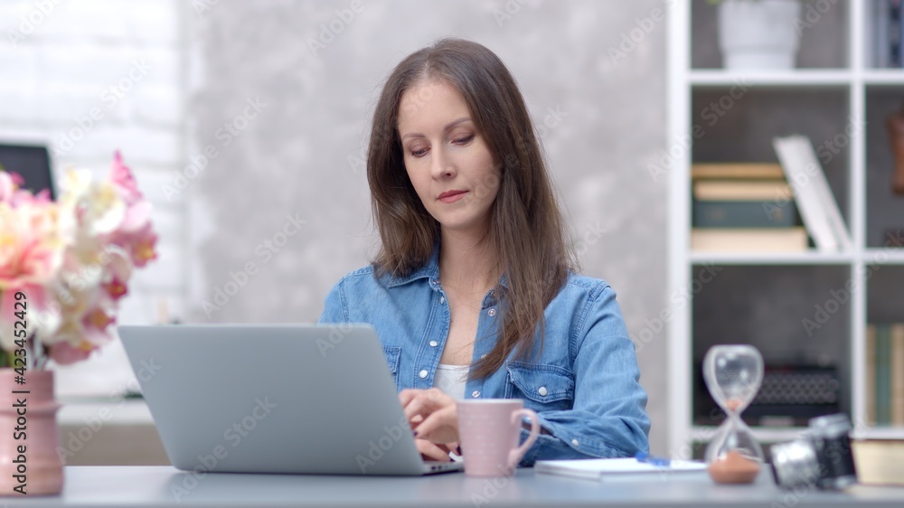 Young woman working online with laptop computer at home sitting at desk. Businesswoman in home office, browsing internet. Young woman working online with laptop computer at home sitting at desk. Businesswoman in home office, browsing internet.