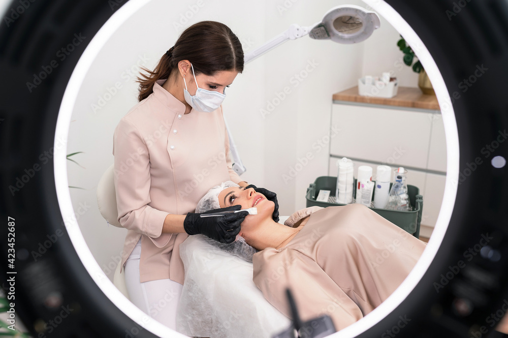 The cosmetologist makes cosmetology procedure to the patient in the cosmetology cabinet with a lamp The cosmetologist makes cosmetology procedure to the patient in the cosmetology cabinet with a lamp