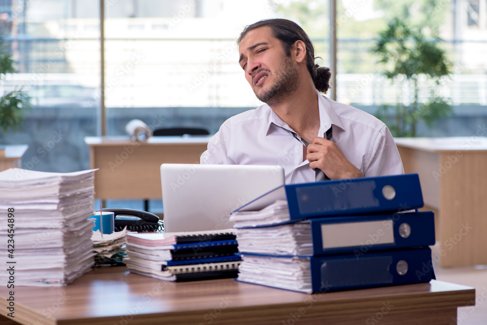 Young male employee unhappy with excessive work in the office Young male employee unhappy with excessive work in the office