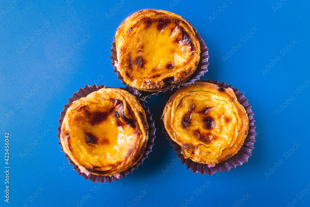 Obraz premium Top view of typical Portuguese dessert pastry Pastéis de Nata - Portuguese egg custard tart, with a blue background