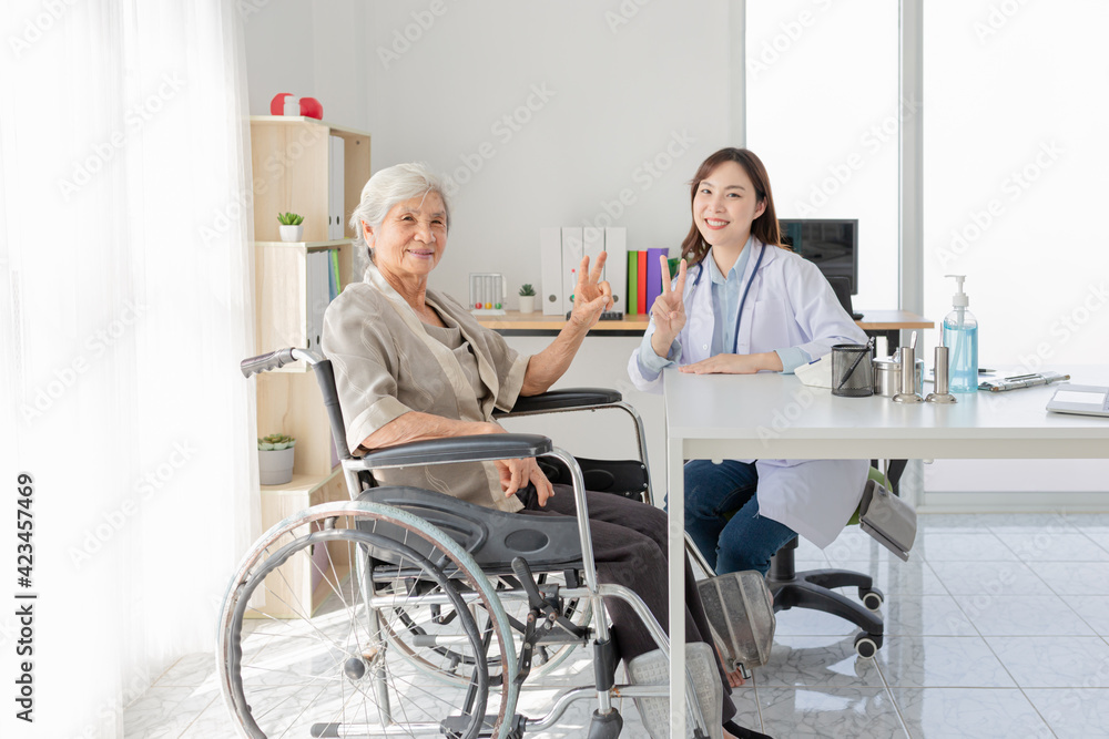 Fototapeta premium asian female doctor and old patient show v sign with hands in hospital, they talk about healthcare promotion and disease screening, elderly health check up