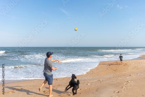 Father throwing football to son on beach during holiday