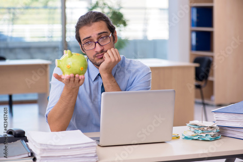 Young male accountant holding piggy bank at workplace