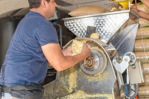 front view of a nixtamal mill while a man takes out the dough that is being produced