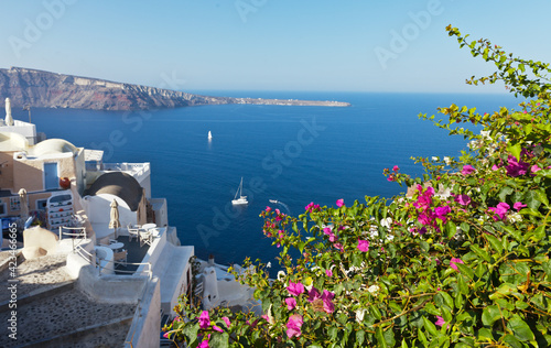 Greece. Santorini island. The beautiful village of Oia with bougainvillea flowers in narrow streets against backdrop of azure waters of the Aegean Sea on sunny day. Seascape. Summer holidays