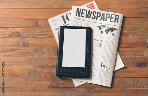 E-reader and newspapers on wooden background