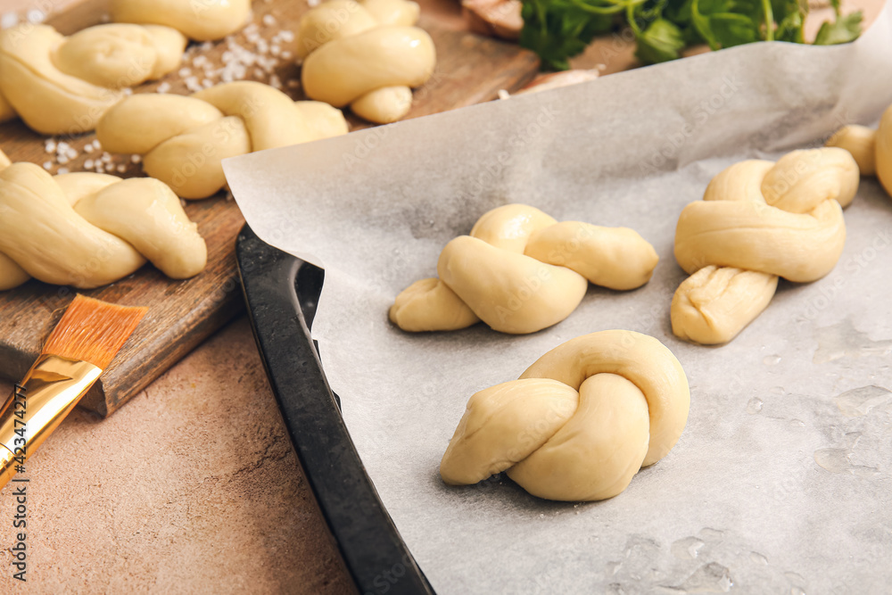 Baking sheet and board with uncooked garlic buns on color background