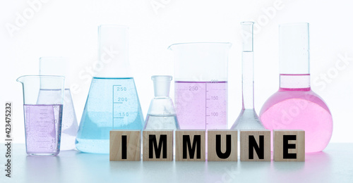 Wooden cubes with the English word IMMUNE written on square blocks. In the background are flasks with multi-colored liquids. Immune to viruses, diseases. Medical concept of protection in a pandemic.