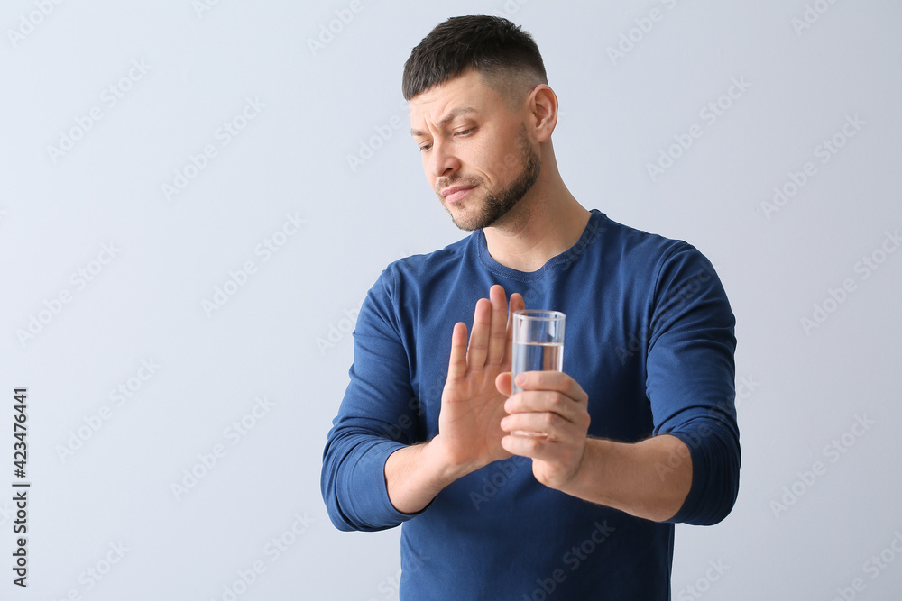 Man with sensitive teeth refusing from glass of cold water on grey background Man with sensitive teeth refusing from glass of cold water on grey background