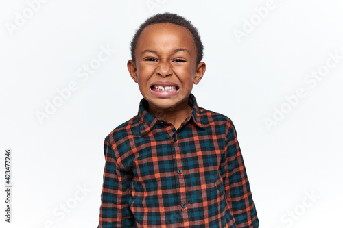 Horizontal shot of mad dissatisfied African boy making angry grimace clenching teeth expressing rage, having furious look, misbehaving. Aggressive enraged child loosing his temper, being irritated