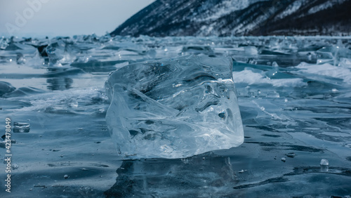 Ice shard close-up. A pale blue transparent shining crystal on the surface of a frozen lake. Reflection. Soft background with many small pieces of ice. Lake Baikal