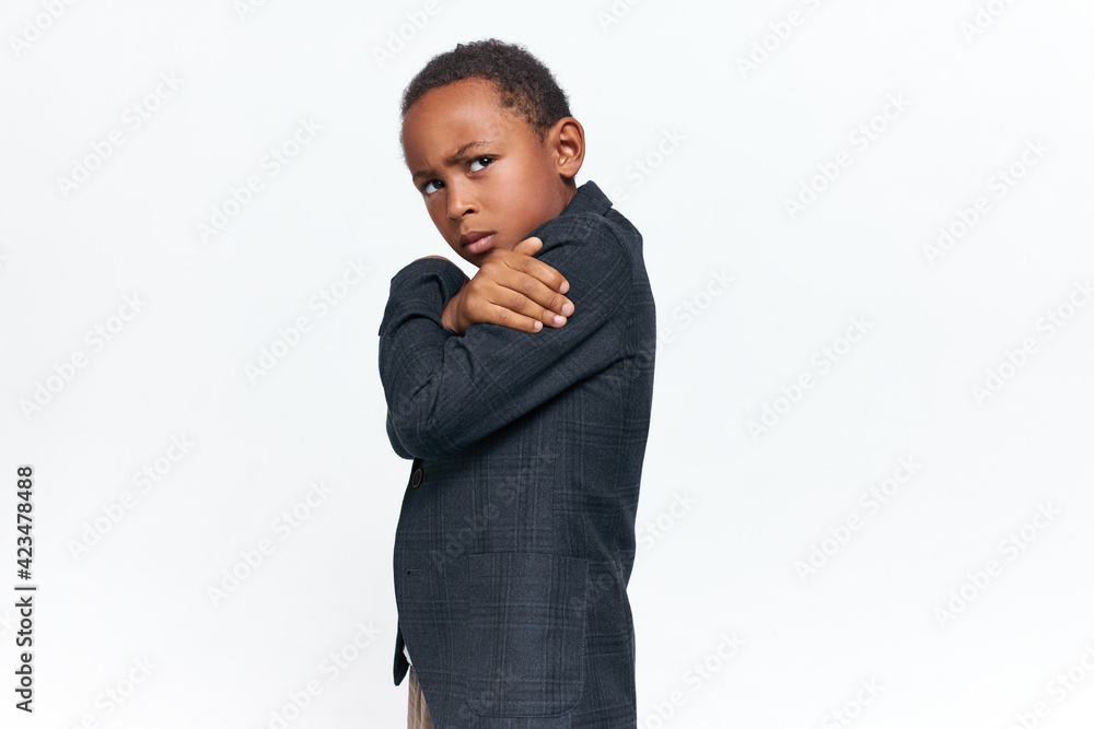Side view image of grumpy dissatisfied African boy wearing elegant trendy jacket posing isolated in closed posture, frowning his eyebrows, being stubborn, misbehaving, refuse to follow rules Side view image of grumpy dissatisfied African boy wearing elegant trendy jacket posing isolated in closed posture, frowning his eyebrows, being stubborn, misbehaving, refuse to follow rules