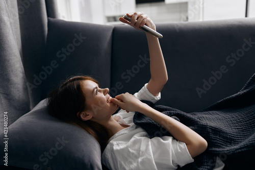 pretty woman with a phone in her hands lies on a sofa indoors