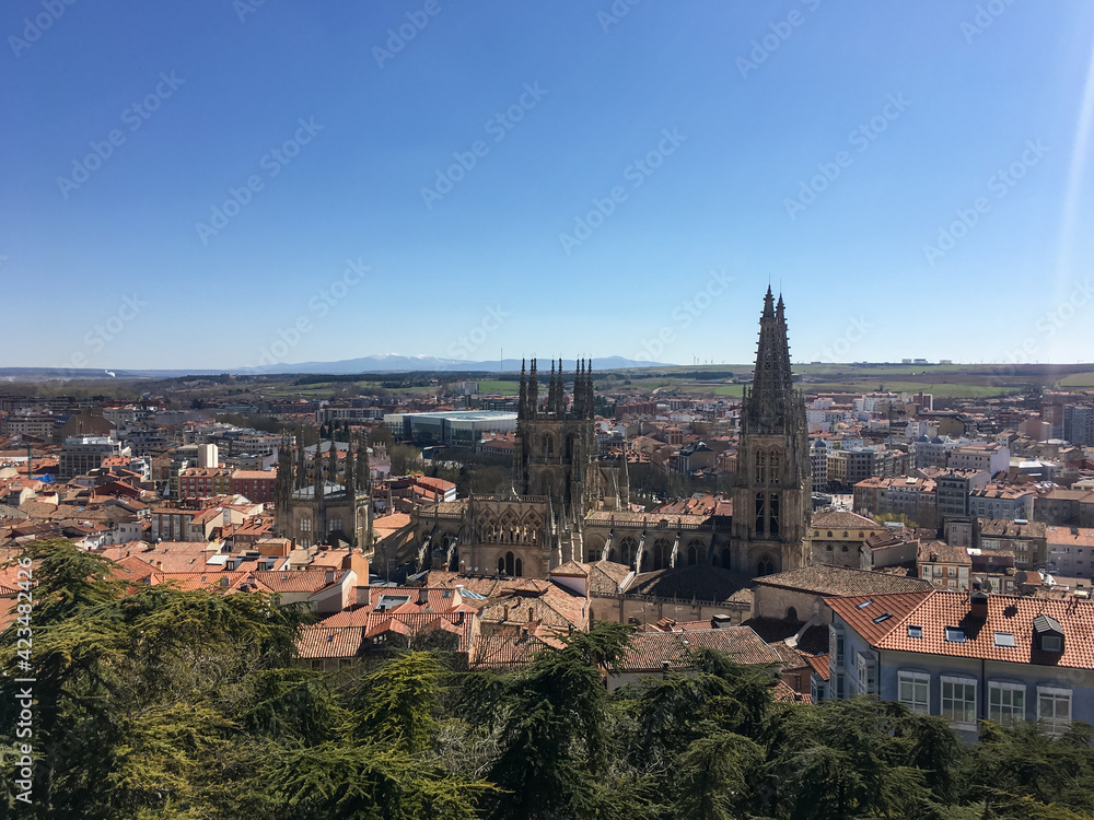 Panoramic view of Burgos with its famous cathedral surrounded by buildings in the foreground and agricultural fields and mountains in the background, on the horizon.