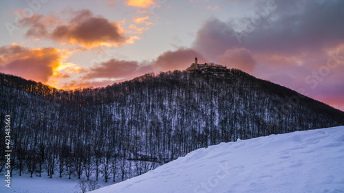 Germany, Magical red burning sky at sunrise in winter with white snow around ancient castle teck on top of a mountain in the swabian alb near stuttgart