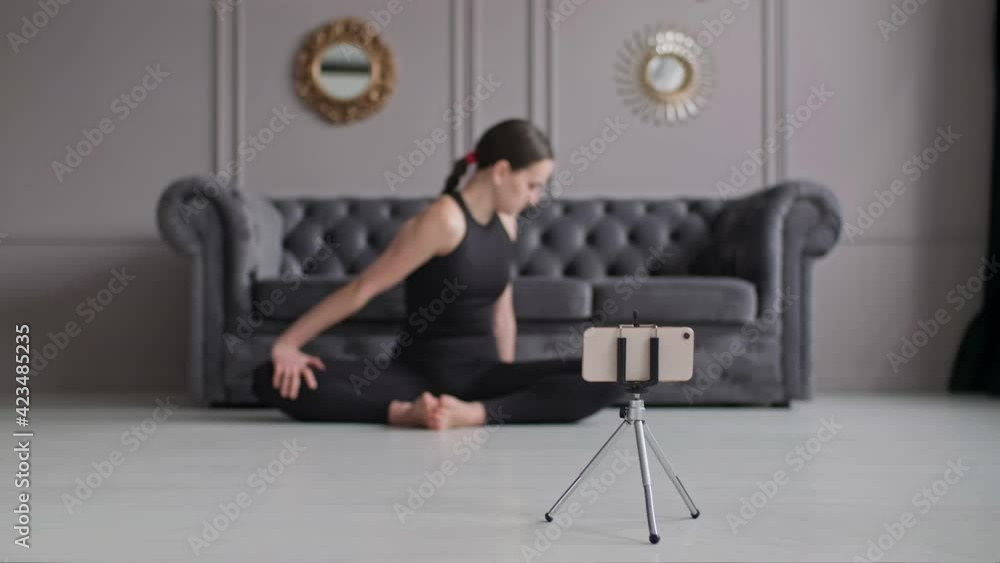 Woman blogger recording stretching exercise at phone. Female practicing yoga at home. Focus on smartphone. Brunette woman streaming online training. Healthy lifestyle at quarantine. Social distance Woman blogger recording stretching exercise at phone. Female practicing yoga at home. Focus on smartphone. Brunette woman streaming online training. Healthy lifestyle at quarantine. Social distance