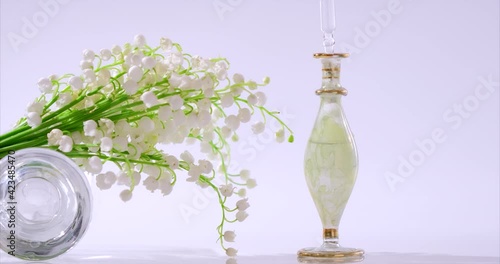 Perfumery. Drops falling from cosmetic pipette to glass bottle with perfume floral oil. Skin and body care of essence flower product. Aroma liquids of Convallaria, lily of the valley, may-lily photo