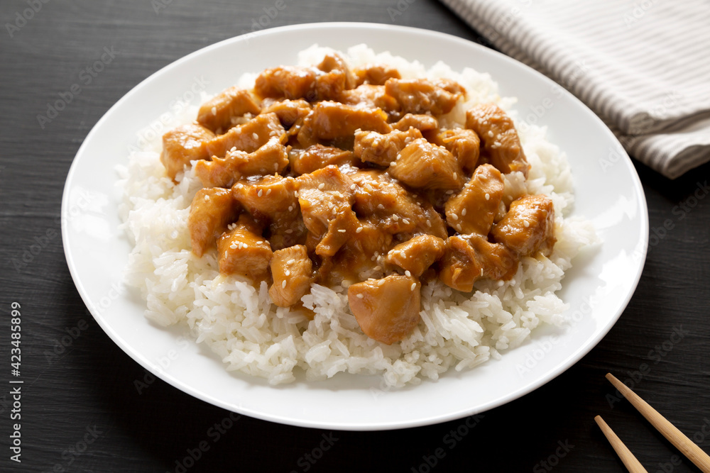 Homemade Orange Chicken with White Rice on a white plate on a black background, side view. Close-up. Homemade Orange Chicken with White Rice on a white plate on a black background, side view. Close-up.