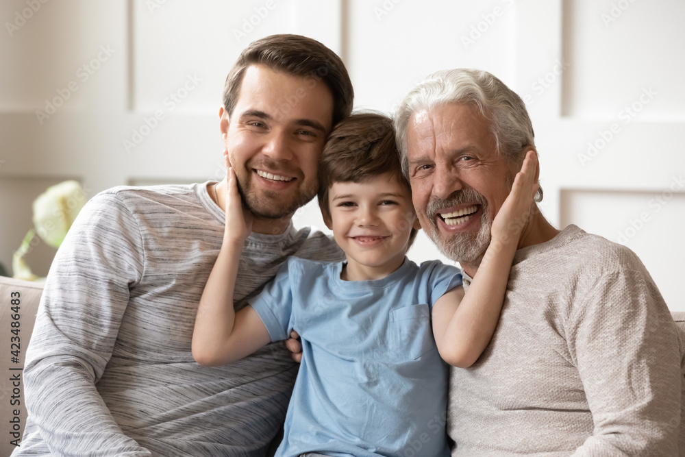 Portrait of happy three generations of Caucasian men sit rest on sofa in living room enjoy family weekend together. Smiling little 8s boy child hug relax with young father and grandfather at home. Portrait of happy three generations of Caucasian men sit rest on sofa in living room enjoy family weekend together. Smiling little 8s boy child hug relax with young father and grandfather at home.