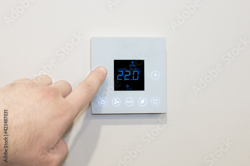 Close-up of a Caucasian male’s hand adjusting a modern wall-mounted digital thermostat. photo