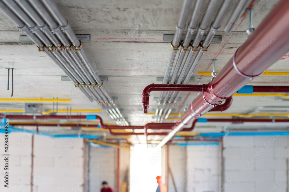 Fire sprinkler system with red pipes is placed to hanging from the ceiling inside of an unfinished new building.Installation of conduits in buildings.Conduit system in building under construction. - obrazy, fototapety, plakaty 