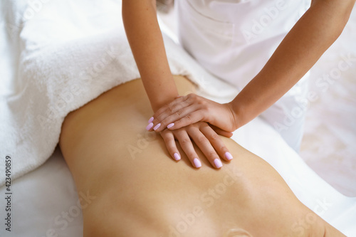 Professional massage therapist massages the back of adult woman lying on massage table  close-up. Lady gets relaxing massage. Concept of body care.