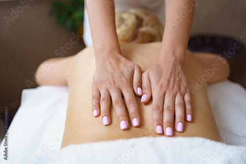 Professional massage therapist massages the back of adult woman lying on massage table  close-up. Lady gets relaxing massage. Concept of body care.