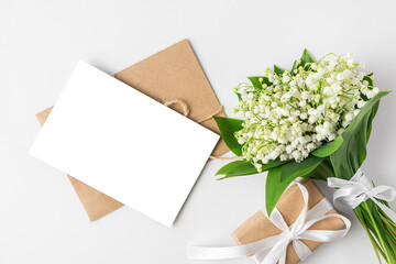 Blank greeting card with spring lily of the valley flowers bouquet and gift box on white background. Flat lay. mock up