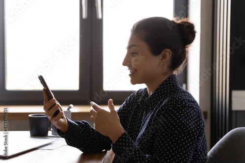Tableau sur toile Side view smiling Indian woman holding phone, making video call to relatives or