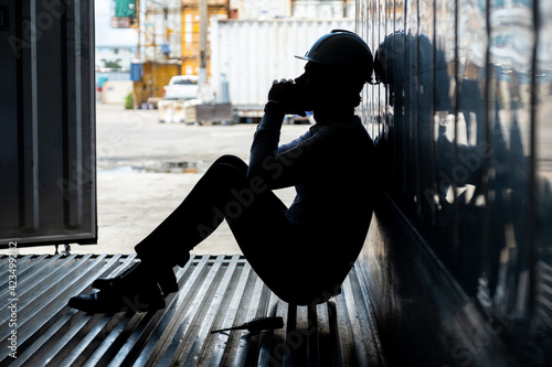 Depressed and tried foreman or businessman sitting inside the container in shipyard logistic factory because losing his job or fired because of mistake. Worker or officer feeling sad and depressed.